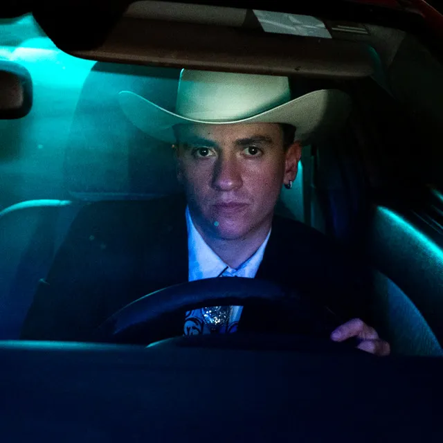 Gallo Armado in a white cowboy hat behind the wheel at night