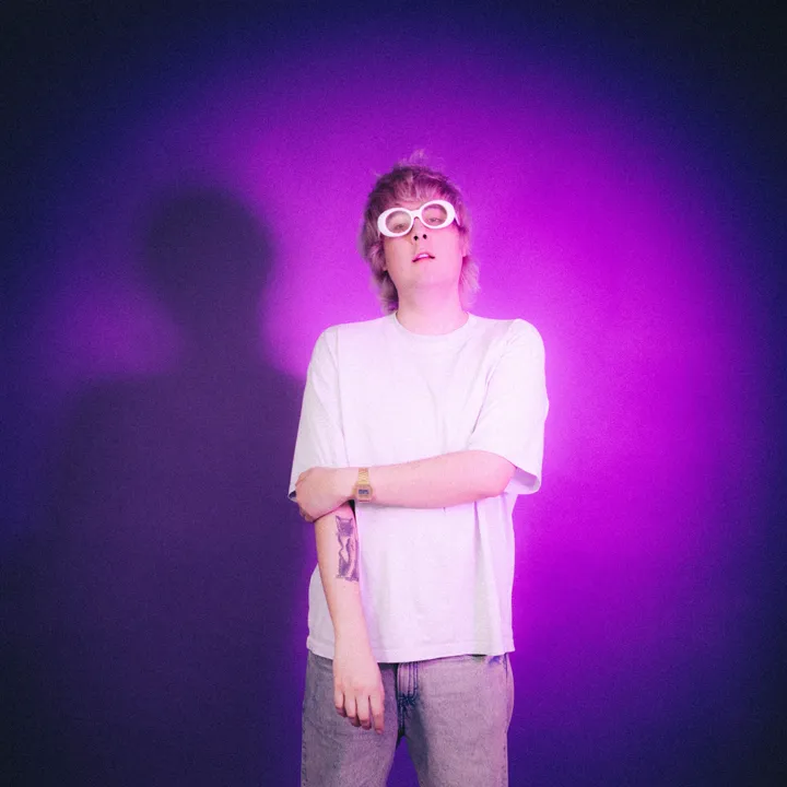 George Rhoads in white sunglasses against a purple backdrop